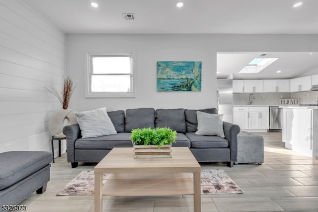 living room featuring a skylight, wood walls, and sink