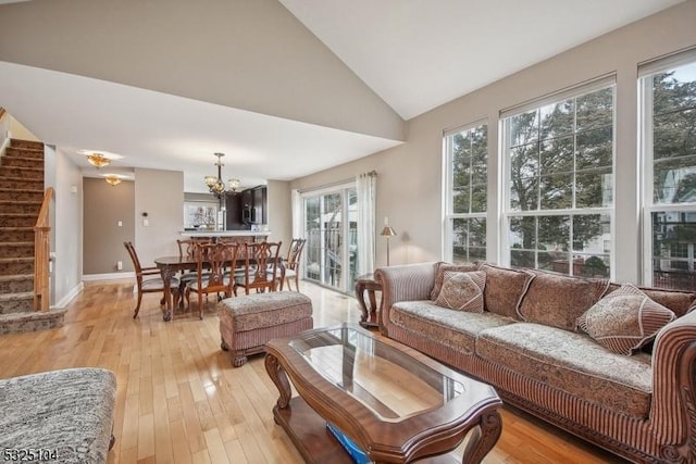 living room with high vaulted ceiling, a healthy amount of sunlight, a notable chandelier, and light hardwood / wood-style floors