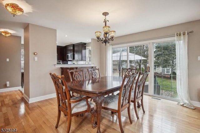 dining space with light hardwood / wood-style floors and a notable chandelier