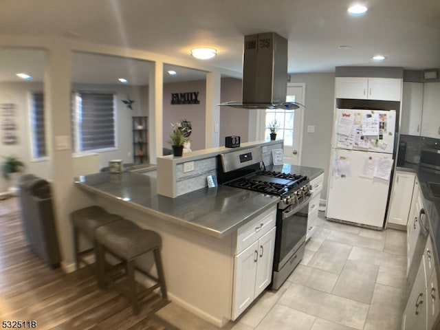 kitchen featuring island range hood, white cabinets, stainless steel range with gas cooktop, white fridge, and a kitchen bar