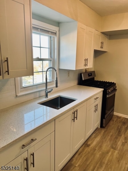 kitchen with white cabinetry, stainless steel gas stove, sink, light stone counters, and light hardwood / wood-style flooring