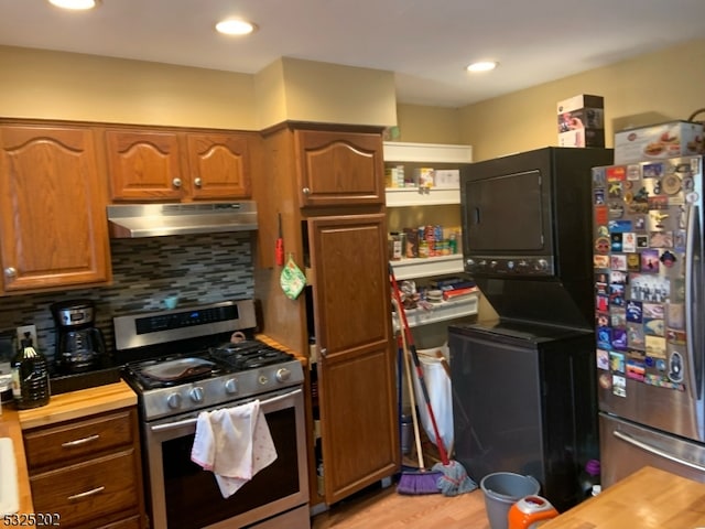 kitchen featuring wood counters, stacked washer and clothes dryer, decorative backsplash, light hardwood / wood-style floors, and stainless steel appliances