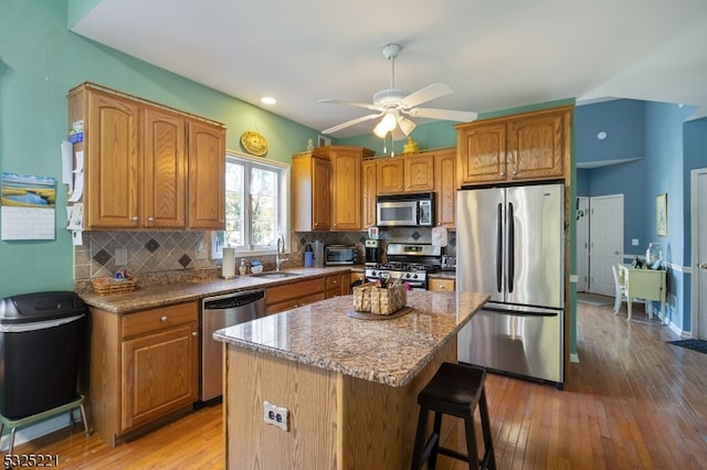 kitchen with backsplash, ceiling fan, light wood-type flooring, a kitchen island, and stainless steel appliances