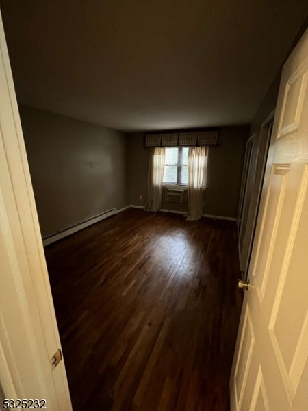 unfurnished room featuring cooling unit, dark hardwood / wood-style floors, and a baseboard heating unit