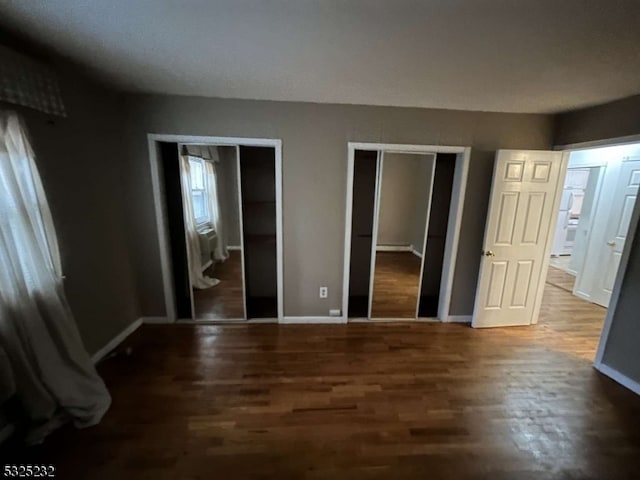 unfurnished bedroom with multiple closets and dark hardwood / wood-style flooring