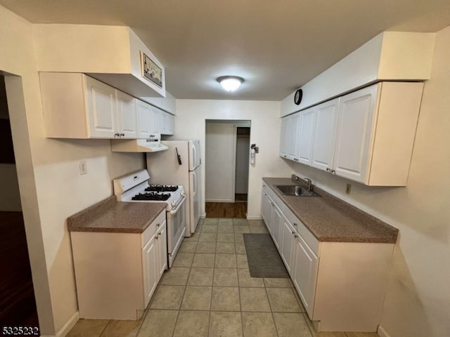 kitchen featuring white gas stove, white cabinets, light tile patterned floors, and sink