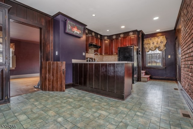 kitchen featuring sink, black fridge, kitchen peninsula, crown molding, and decorative backsplash