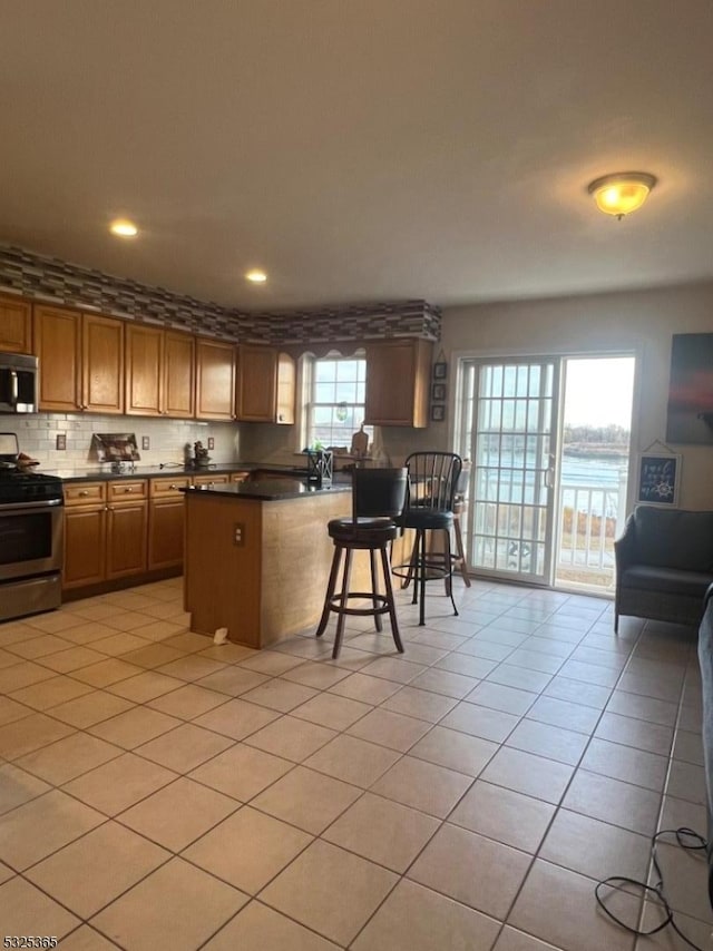 kitchen with a breakfast bar, decorative backsplash, light tile patterned flooring, kitchen peninsula, and stainless steel appliances