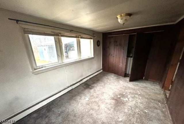 unfurnished bedroom featuring wood walls, a closet, and a baseboard heating unit