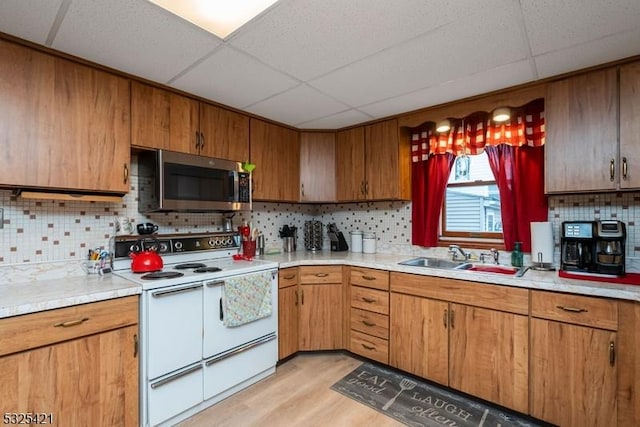 kitchen with sink, double oven range, a drop ceiling, decorative backsplash, and light wood-type flooring