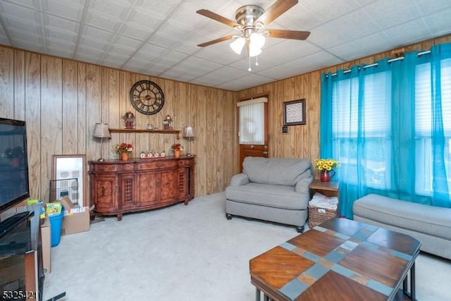 living room featuring ceiling fan, light colored carpet, and wood walls