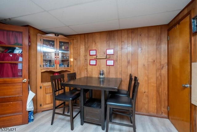 dining room with a paneled ceiling, light hardwood / wood-style flooring, and wood walls