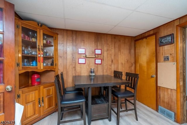 dining room featuring wood walls, light hardwood / wood-style flooring, and a drop ceiling