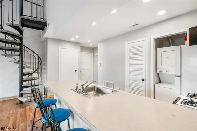 kitchen with sink, dark hardwood / wood-style floors, white fridge, a breakfast bar, and stacked washer and clothes dryer