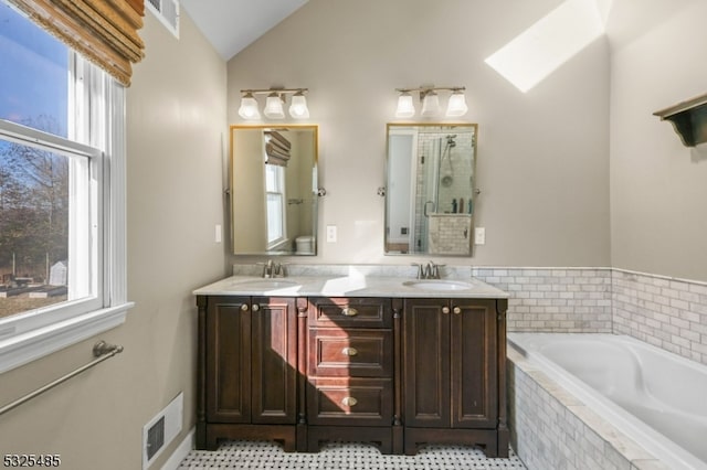 bathroom with tile patterned floors, vaulted ceiling with skylight, vanity, and independent shower and bath