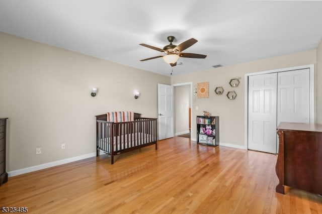 bedroom with ceiling fan, light hardwood / wood-style floors, a closet, and a nursery area