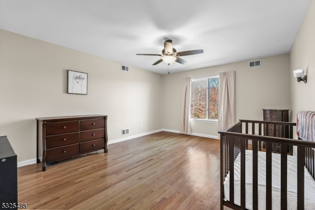 bedroom with a nursery area, light hardwood / wood-style flooring, and ceiling fan