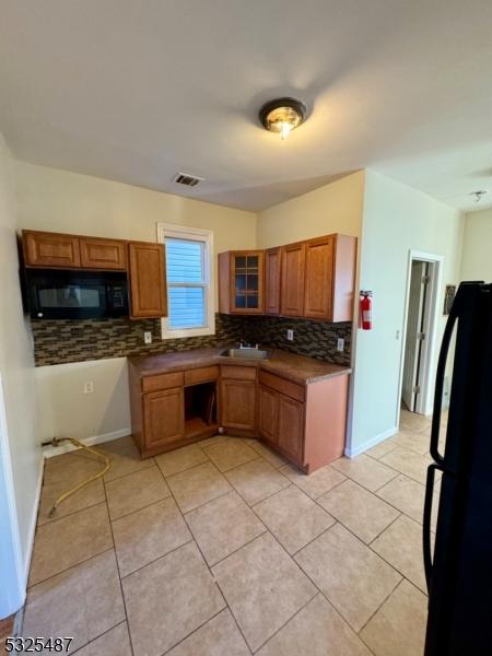 kitchen featuring decorative backsplash, sink, light tile patterned floors, and black appliances