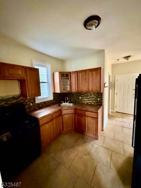 kitchen with backsplash, sink, light tile patterned floors, and black appliances