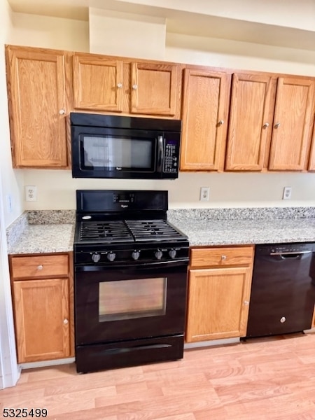 kitchen with light hardwood / wood-style floors, light stone counters, and black appliances