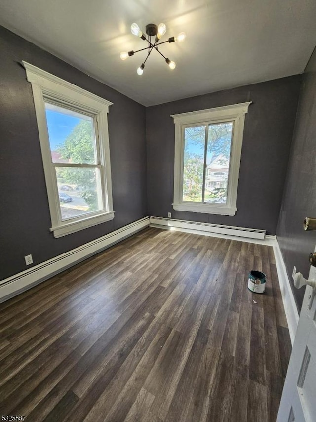 spare room featuring a wealth of natural light, dark wood-type flooring, a baseboard radiator, and an inviting chandelier