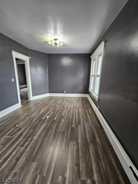 unfurnished room with baseboard heating and dark wood-type flooring