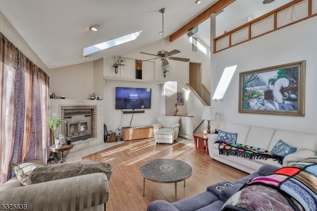 living room featuring hardwood / wood-style floors, a skylight, ceiling fan, a fireplace, and beamed ceiling