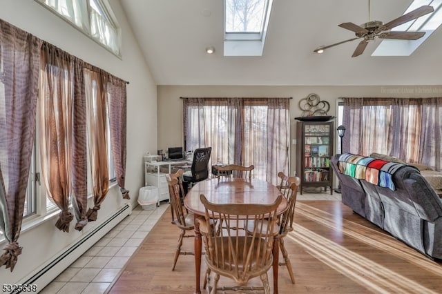 dining room featuring high vaulted ceiling, a skylight, light hardwood / wood-style flooring, ceiling fan, and baseboard heating