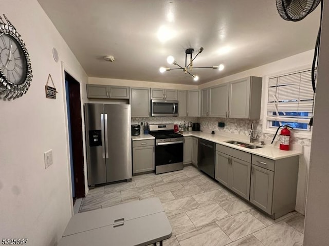 kitchen with backsplash, an inviting chandelier, sink, gray cabinets, and stainless steel appliances