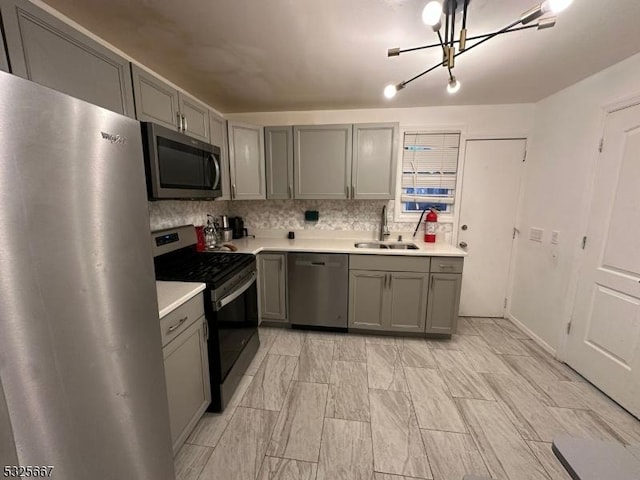 kitchen featuring gray cabinetry, a notable chandelier, sink, and stainless steel appliances