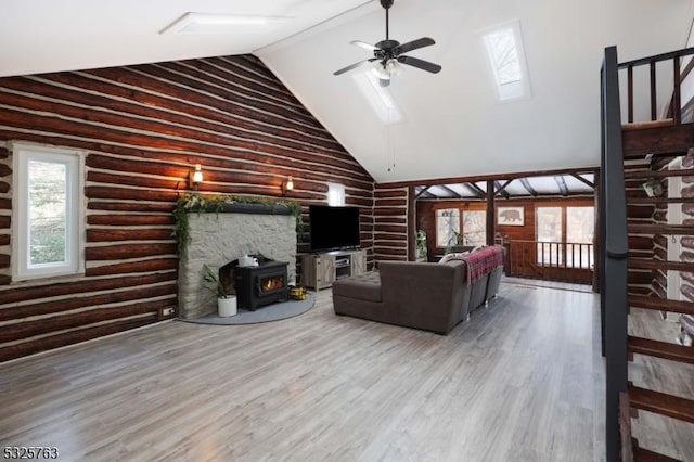 living room featuring log walls, a ceiling fan, a wood stove, wood finished floors, and high vaulted ceiling