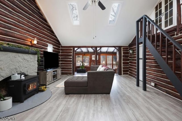 living area featuring a ceiling fan, stairway, a wood stove, light wood-style floors, and high vaulted ceiling