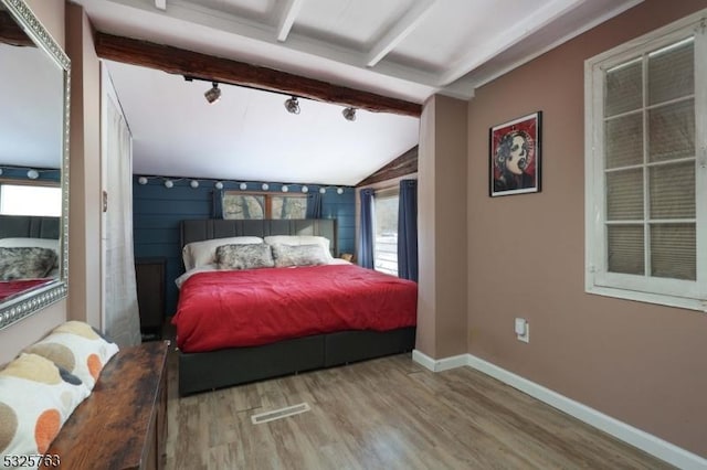 bedroom with vaulted ceiling with beams, wood finished floors, visible vents, baseboards, and rail lighting