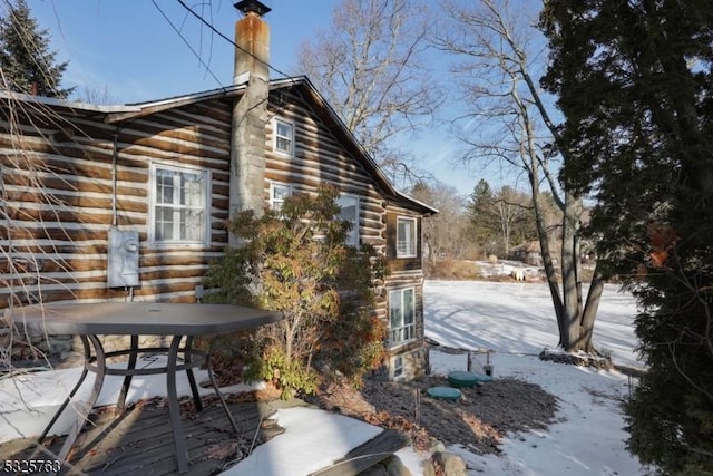 view of snowy exterior featuring a chimney and log siding