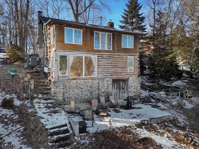 view of snowy exterior with central air condition unit, stone siding, and a chimney