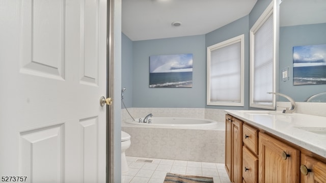 bathroom featuring tile patterned flooring, vanity, a relaxing tiled tub, and toilet