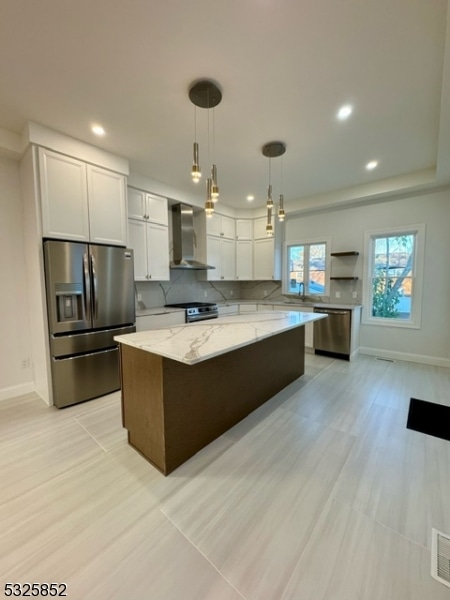 kitchen featuring appliances with stainless steel finishes, a center island, white cabinetry, and wall chimney range hood