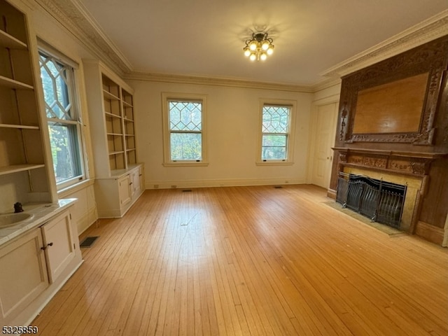 unfurnished living room featuring built in features, light wood-type flooring, and ornamental molding