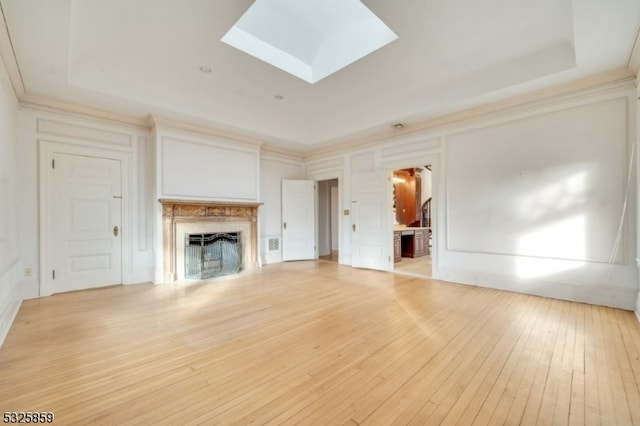 unfurnished living room with light hardwood / wood-style flooring, a tray ceiling, and a skylight