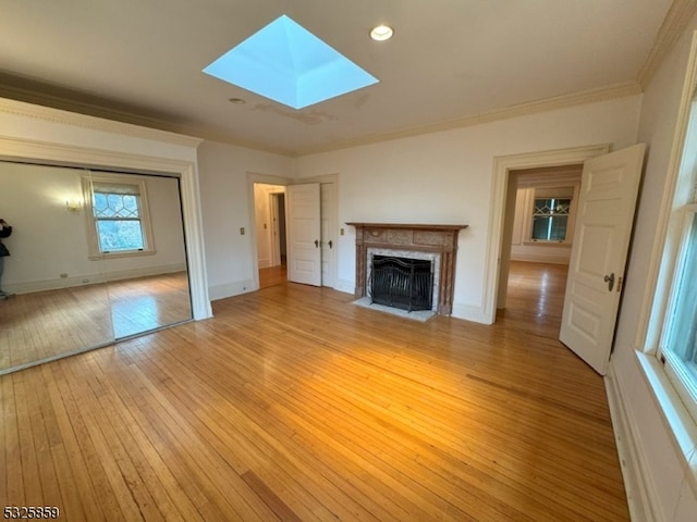 unfurnished living room with light wood-type flooring, a skylight, and ornamental molding