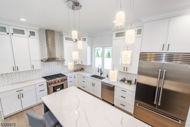 kitchen featuring sink, white cabinets, hanging light fixtures, high end appliances, and wall chimney exhaust hood