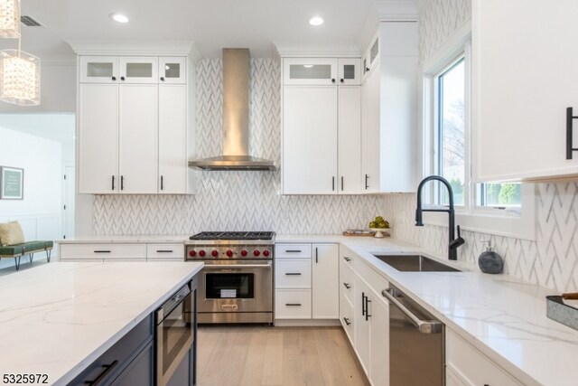 kitchen featuring sink, white cabinets, hanging light fixtures, stainless steel appliances, and wall chimney exhaust hood