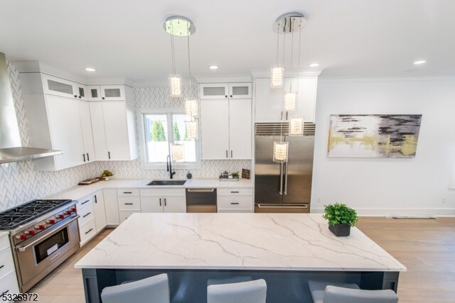 kitchen featuring a breakfast bar area, high end appliances, pendant lighting, wall chimney range hood, and white cabinets