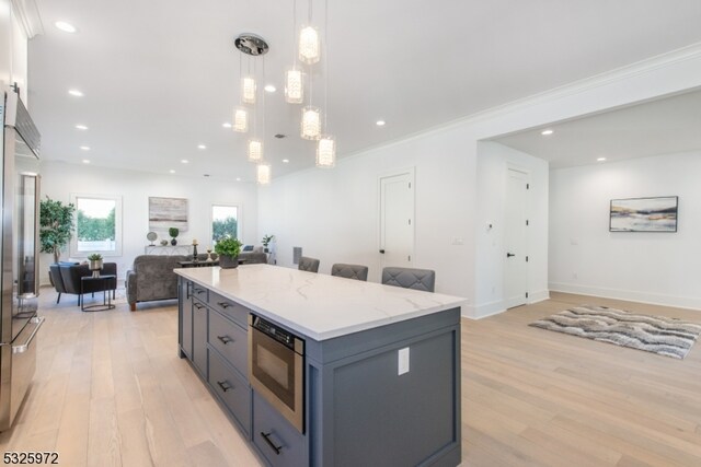 kitchen with appliances with stainless steel finishes, a kitchen island, hanging light fixtures, and light wood-type flooring