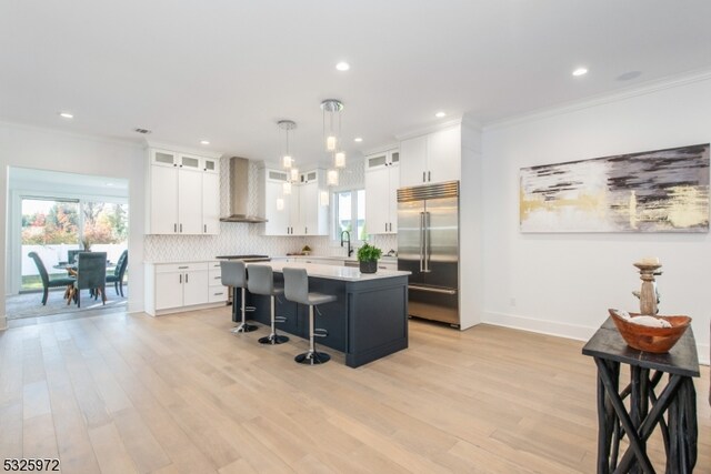 kitchen with white cabinetry, wall chimney range hood, a kitchen island, and built in refrigerator