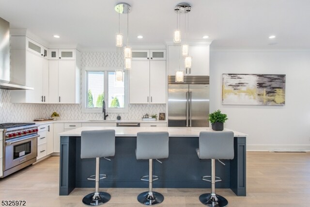 kitchen featuring sink, high end appliances, a kitchen island, white cabinets, and wall chimney range hood