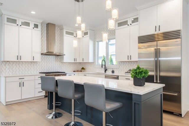 kitchen featuring white cabinetry, a kitchen island, wall chimney exhaust hood, and appliances with stainless steel finishes