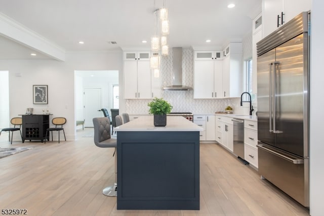 kitchen featuring wall chimney range hood, stainless steel appliances, and white cabinets