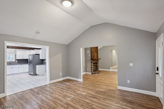 unfurnished living room featuring sink, light wood-type flooring, a fireplace, and vaulted ceiling