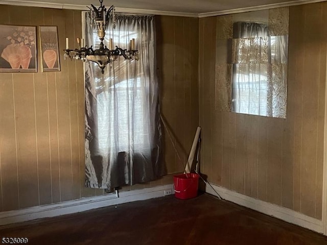 unfurnished dining area with a wealth of natural light, wooden walls, crown molding, and a notable chandelier